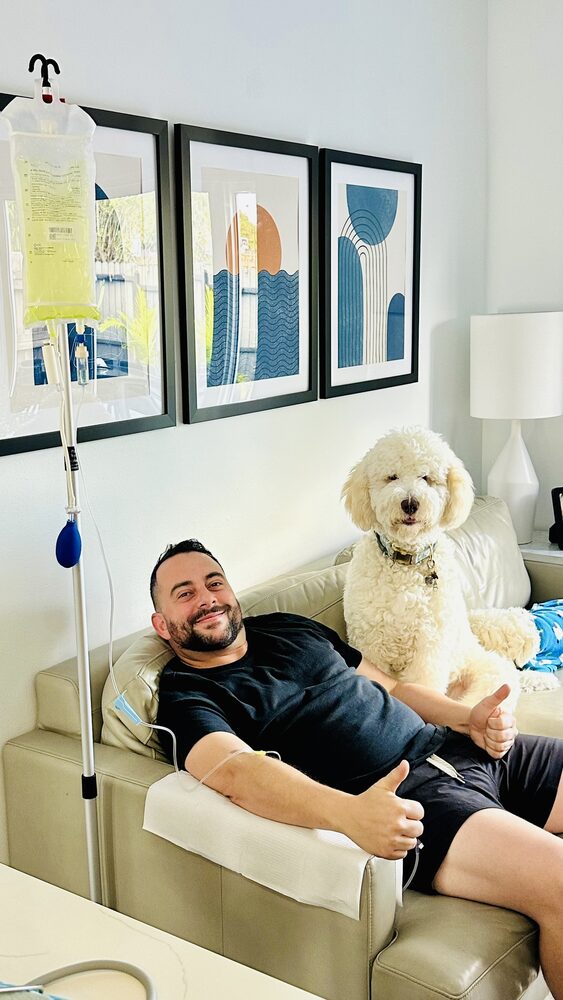 A client relaxing at home during an IV infusion with his dog